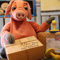 Eine Schweinepuppe, die einen Huf auf ein Postpaket legt.