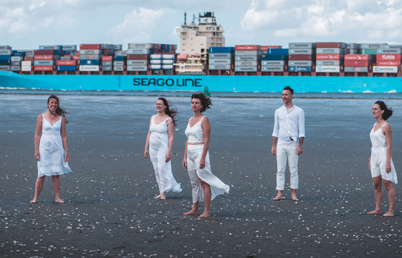 Die Künstler am Strand. Im Hintergrund ein Frachtschiff