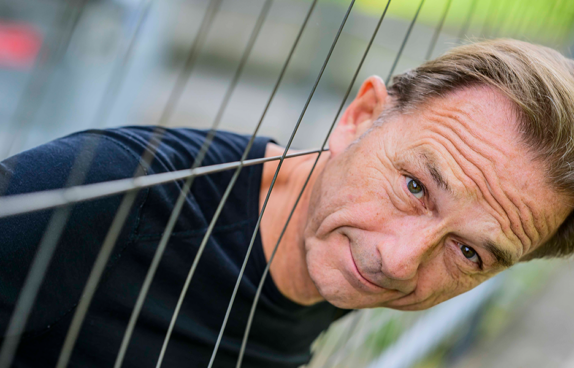 Fritz Eckengag steckt seinen Kopf durch die Gitter eines Bauzauns.