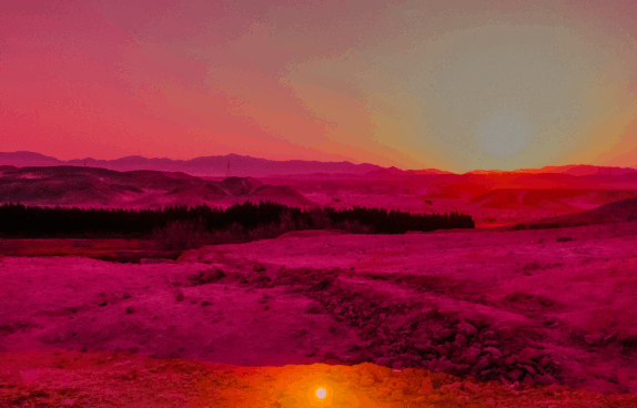 Eine weite, karge Landschaft bei Sonnenuntergang. Der Himmel leuchtet intensiv in Rosa-, Orange- und Gelbtönen. In der Ferne sind dunkle Hügel und eine Baumreihe zu sehen, während der Vordergrund von rötlich-violettem Gestein und Sand bedeckt ist. Die Atmosphäre wirkt surreal und farbverfremdet, fast außerirdisch.