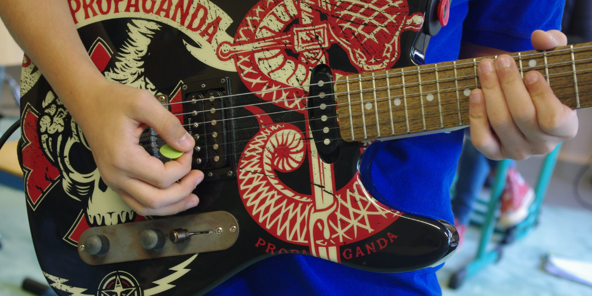 Foto für den Bandworkshop im Rahmen der Sommerwerkstatt 2026. Ein Kind spielt Gitarre.
